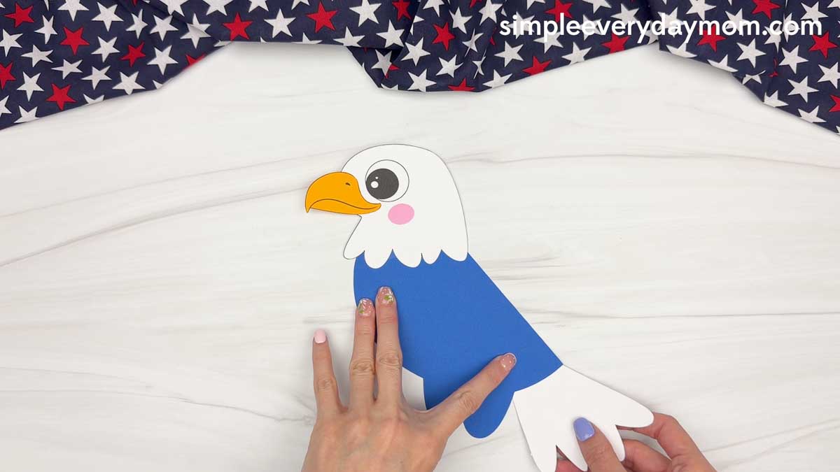 Hands attaching the white tail feathers to the back of an American eagle handprint craft.