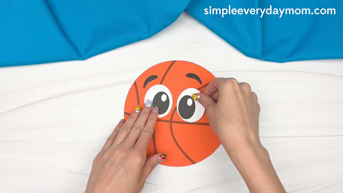 Hands gluing eyes onto a basketball paper craft for a Father’s Day activity.