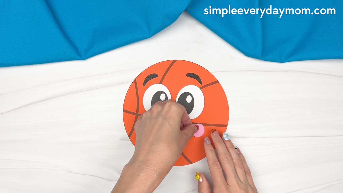 Hands gluing a pink cheek onto a basketball Father’s Day paper craft.