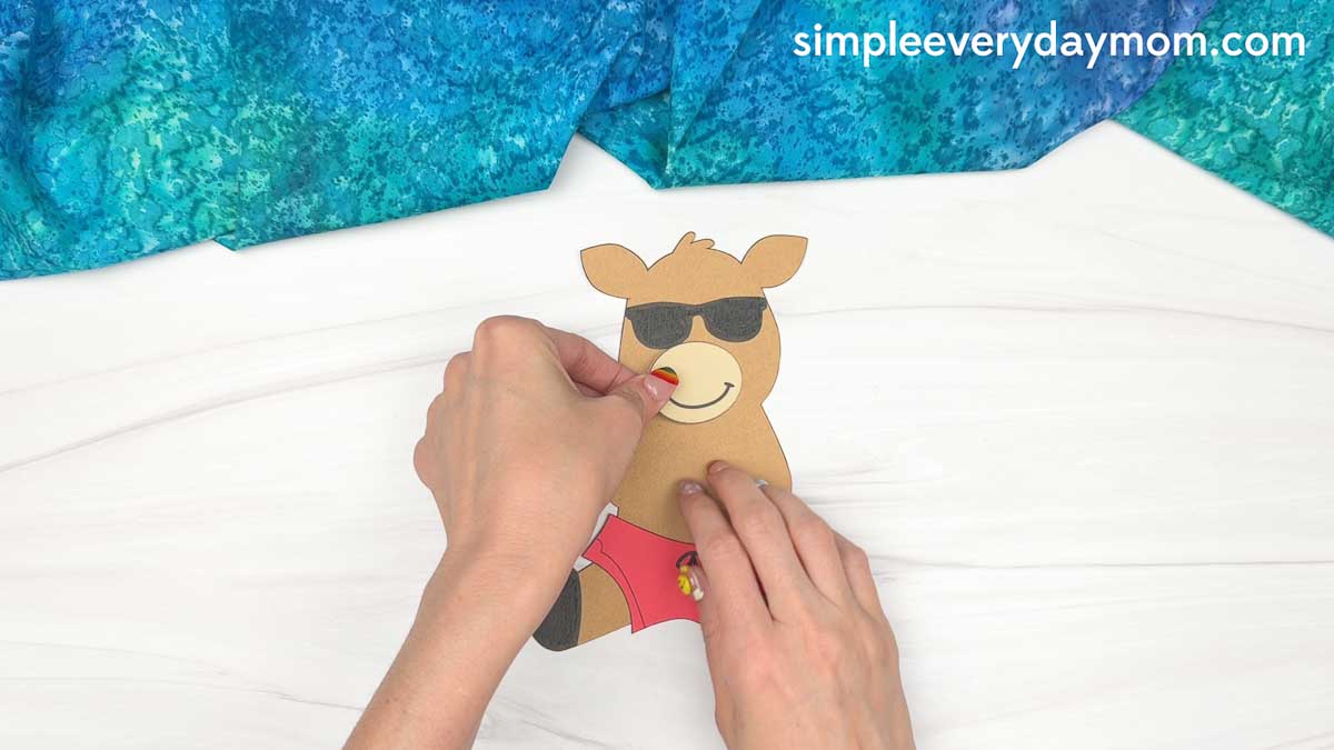 Hands attaching the reindeer's muzzle piece to the face while assembling a reindeer summer craft.