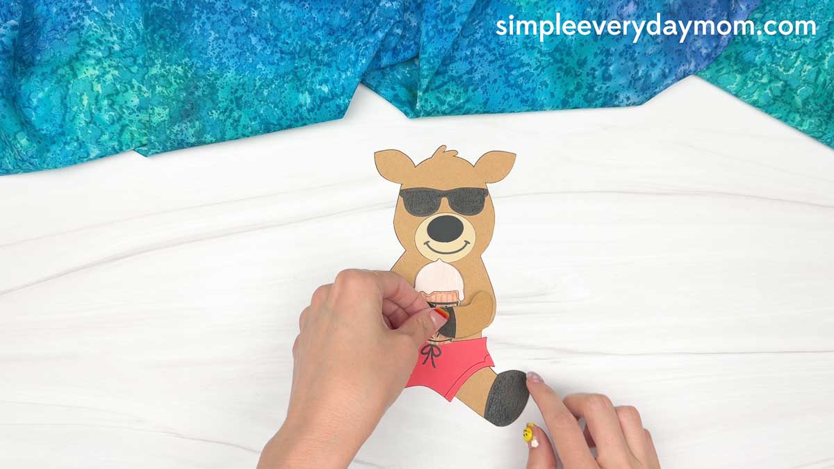 Hands attaching the reindeer's arm cutout around the ice cream cone while assembling a reindeer summer craft.