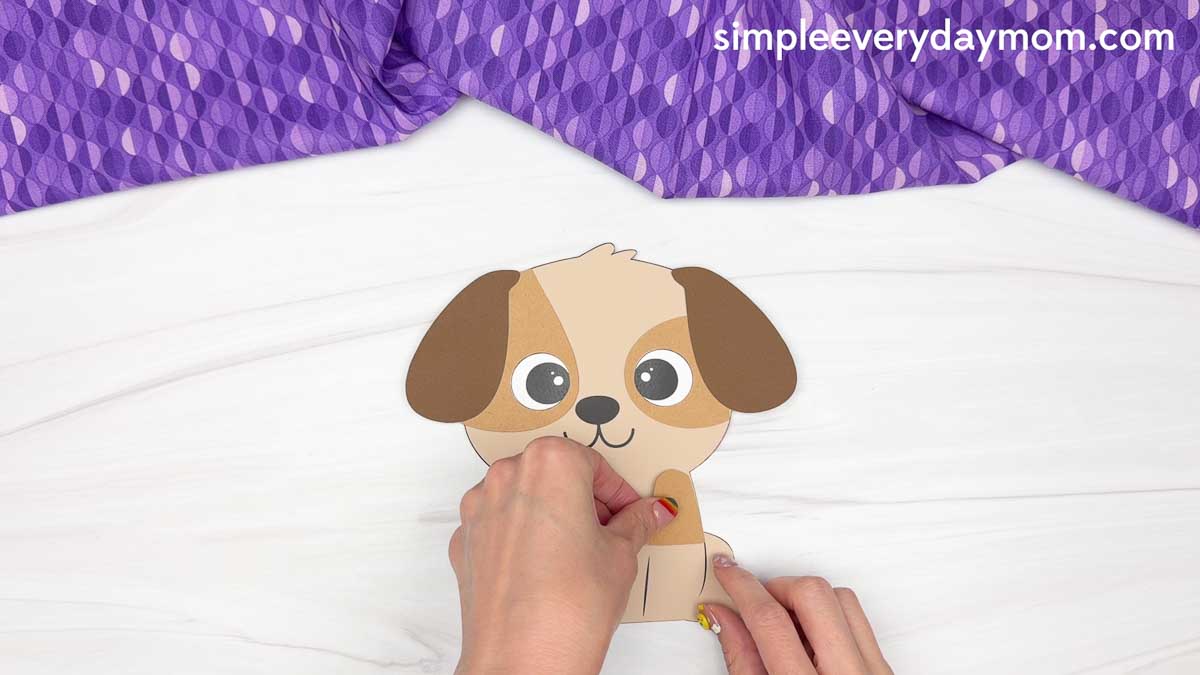 Hands attaching a paper patch to the puppy’s body for a Father's Day dog craft activity