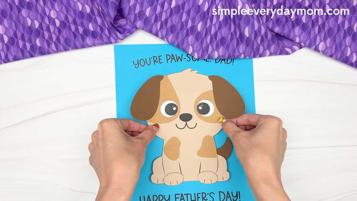 Hands placing a completed puppy craft onto a blue Father’s Day card with a paw-some message for dad