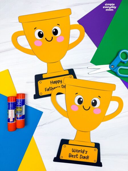 A completed craft showing two smiling Father’s Day trophy crafts with craft supplies and colorful paper.