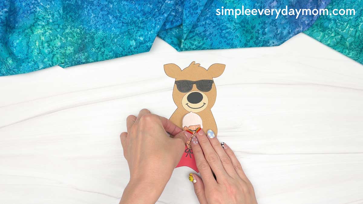Hands attaching an ice cream cone cutout to the reindeer's hands while assembling a reindeer summer craft.