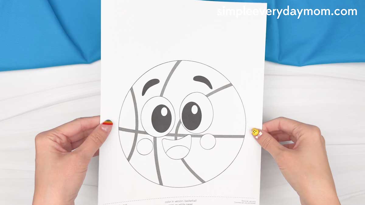 Hands holding a printable basketball character template for a Father’s Day craft activity.