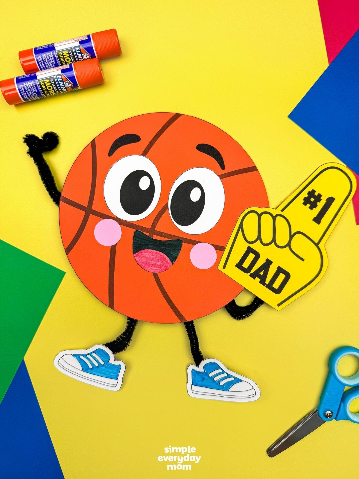 A completed craft of a basketball Father’s Day character with a number one dad foam finger and colorful craft supplies.