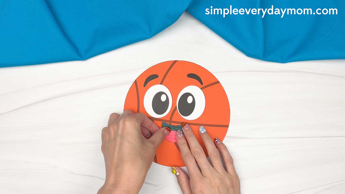 Hands attaching the mouth piece to a basketball paper craft for Father’s Day.