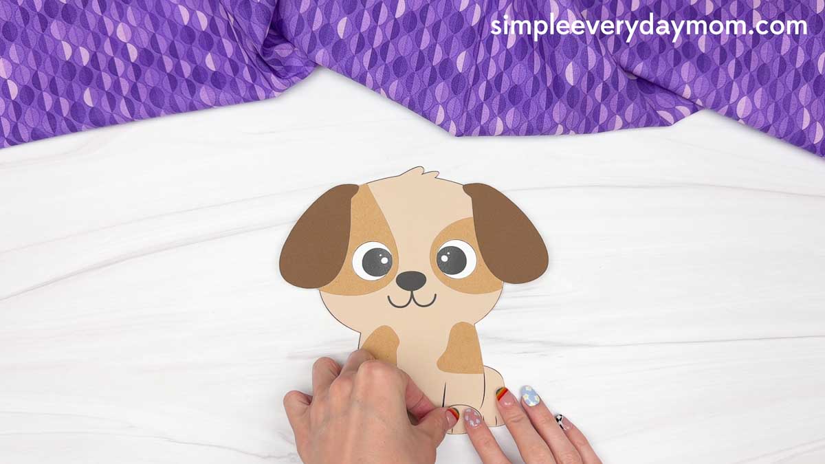 Hands placing the final paper patch onto a puppy craft for a Father's Day dog craft activity