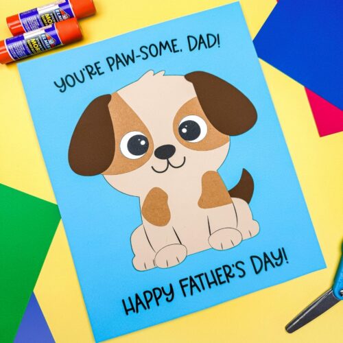 A completed craft featuring a puppy Father’s Day card with colorful paper supplies and glue sticks on a craft table