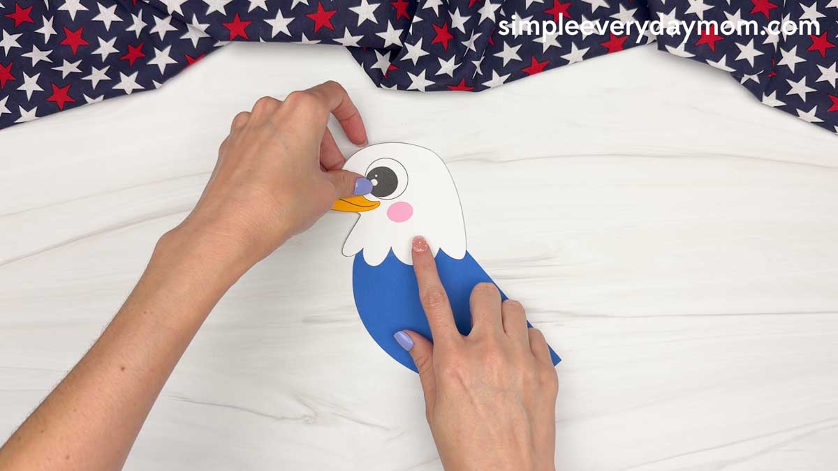 Hands attaching the eagle head to the blue handprint body for an American eagle handprint craft.