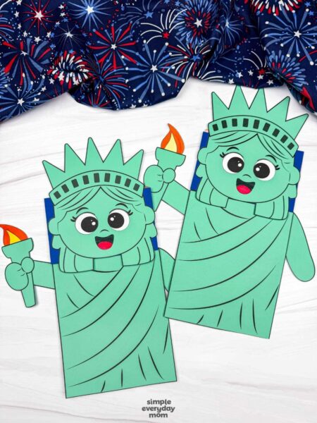 A completed craft showing two Statue of Liberty paper bag puppet crafts with torches on a white tabletop.