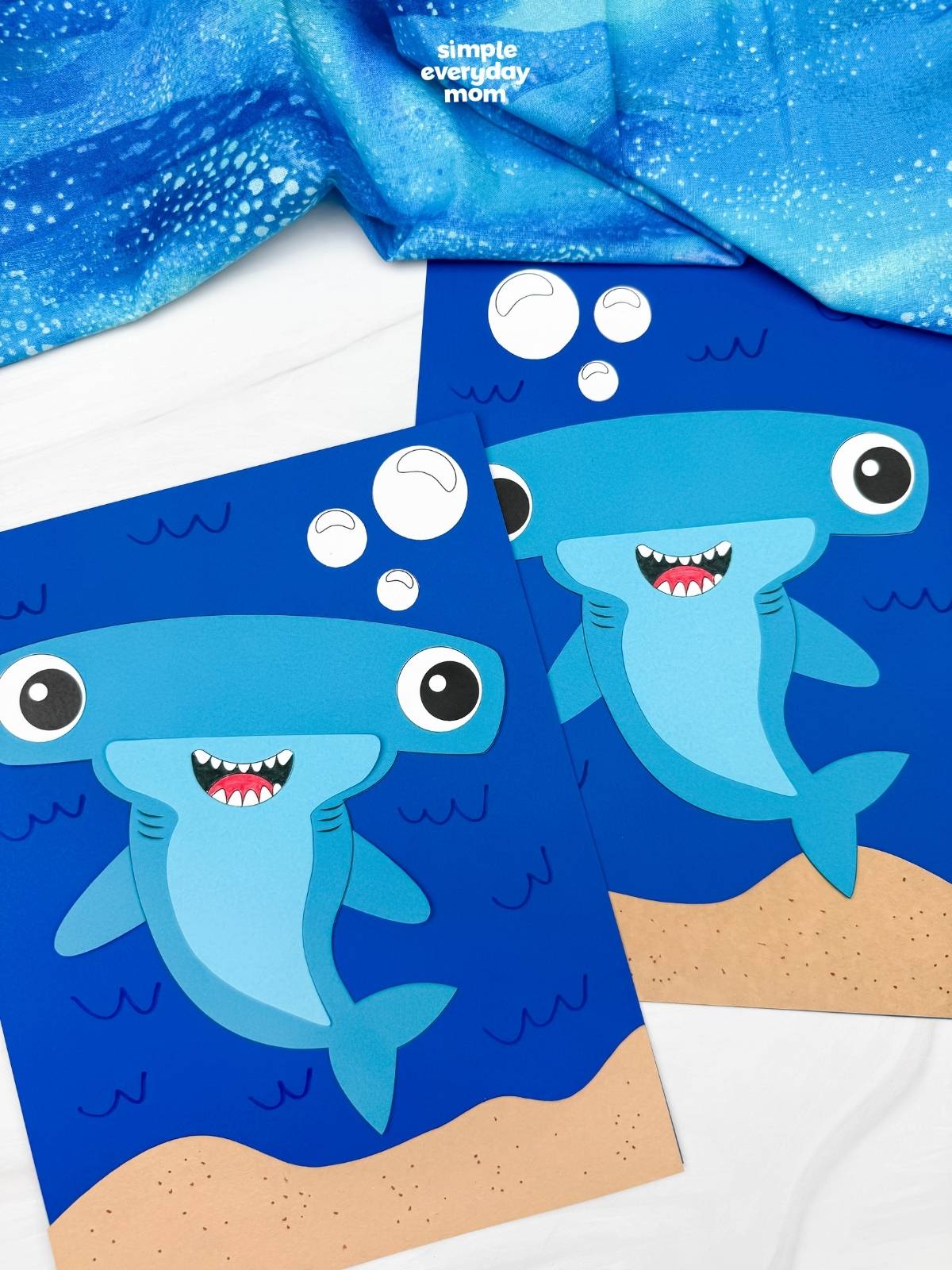 A completed hammerhead shark craft displayed on blue underwater backgrounds with bubbles and sandy ocean floors.