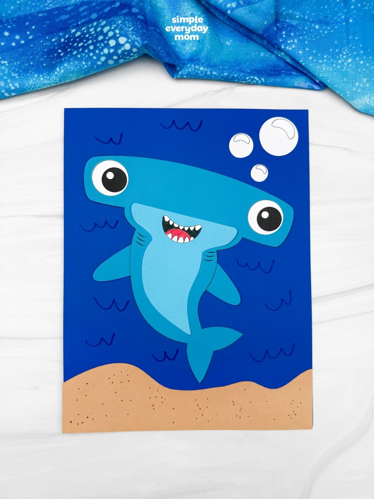 A completed hammerhead shark craft on a blue underwater background with bubbles, ocean waves, and a sandy seafloor.