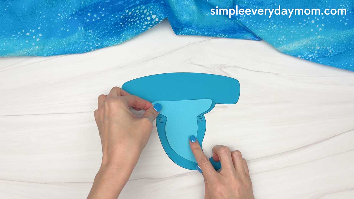 Hands assembling a blue hammerhead shark craft by attaching the body piece to the shark head.
