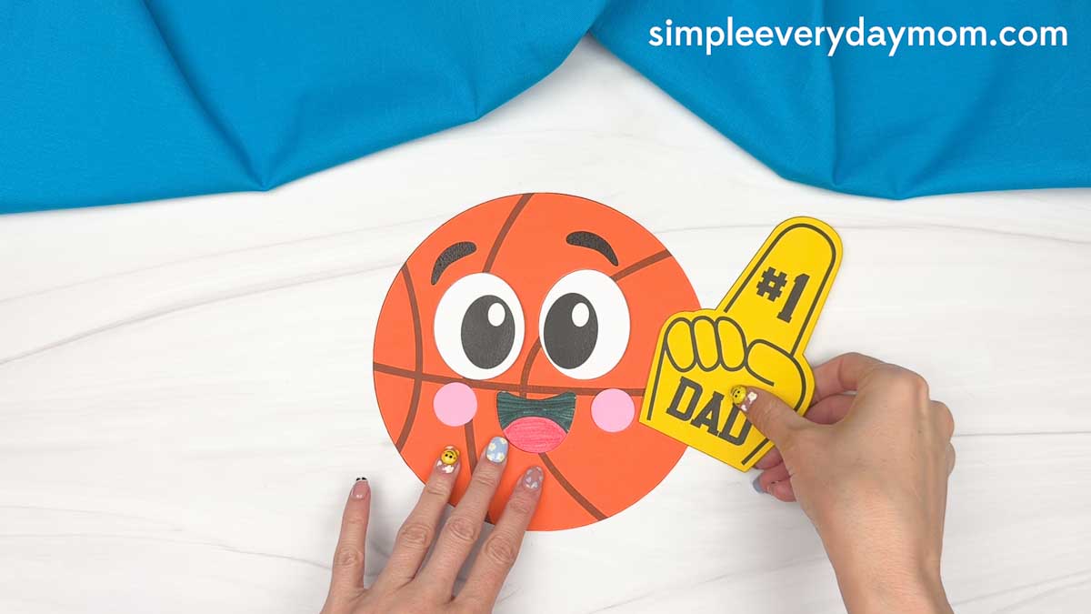 Hands placing a number one dad foam finger next to a basketball Father’s Day paper craft.