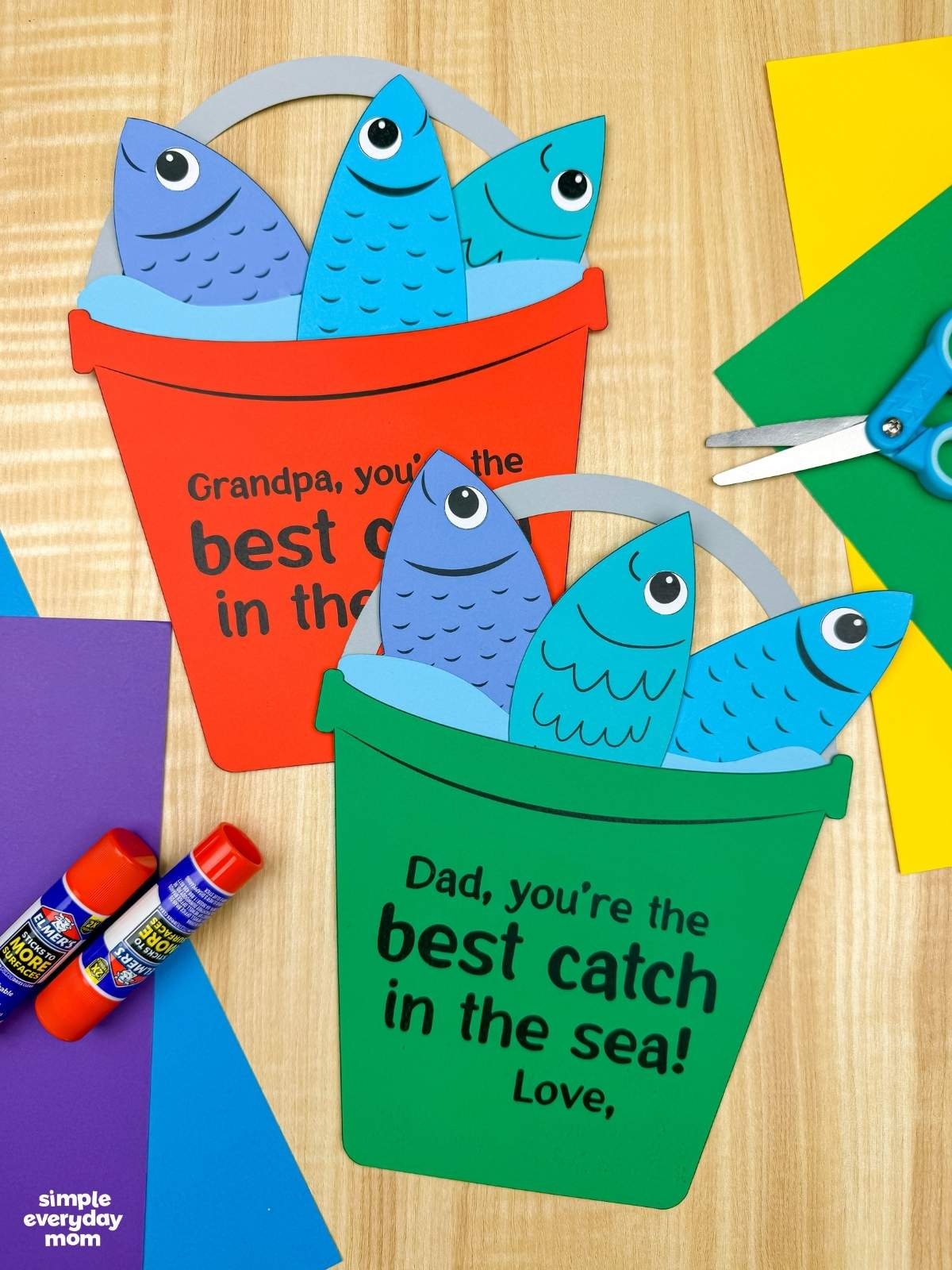 A completed Father’s Day fishing bucket craft for dads and grandpas surrounded by colorful cardstock paper and craft supplies.