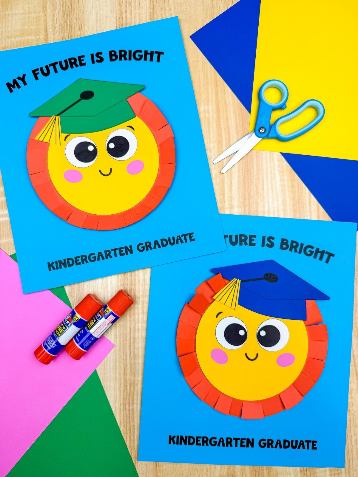 A completed craft display of sun graduation cards with smiling suns wearing colorful graduation caps surrounded by scissors, glue sticks, and bright paper sheets