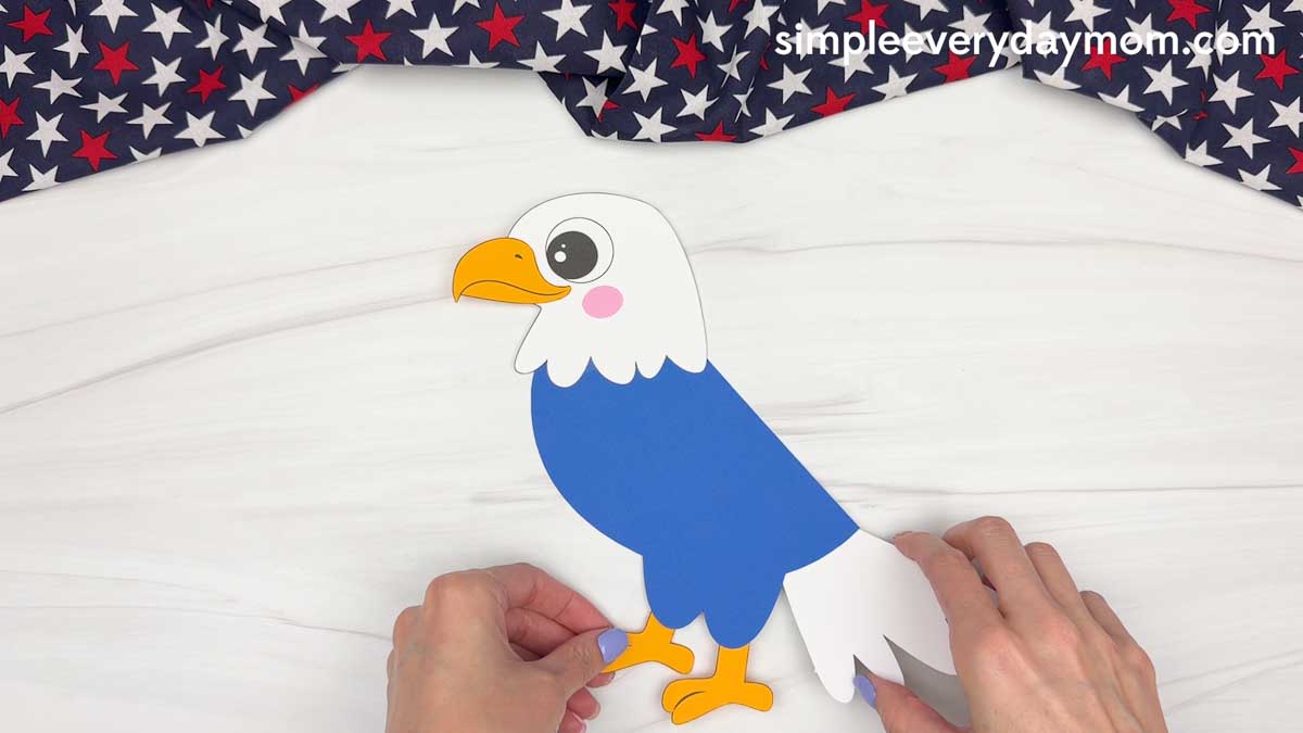 Hands attaching the yellow eagle feet to the bottom of an American eagle handprint craft.