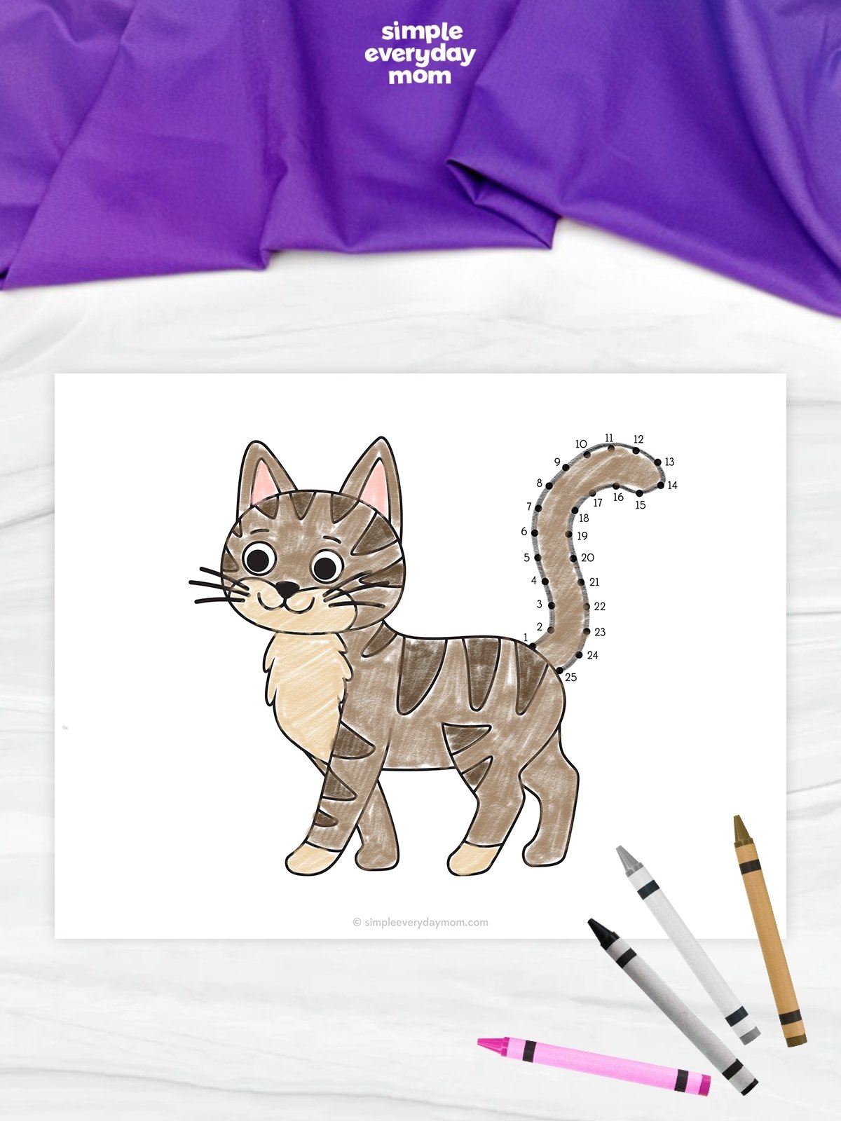 This image shows a completed cat connect-the-dots worksheet displayed on a light marble-like background. The brown-striped cat is colored with soft shades of brown and cream, while numbered dots outline its curved tail for the connect-the-dots activity. Several crayons are scattered in the lower-right corner, and a purple fabric with the Simple Everyday Mom logo appears across the top of the image.