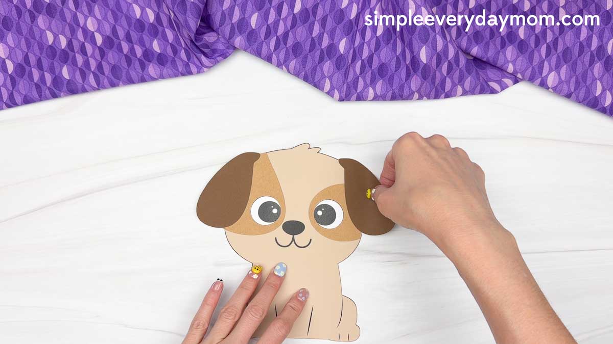 Hands attaching floppy ears to a paper puppy craft for a Father's Day dog craft activity