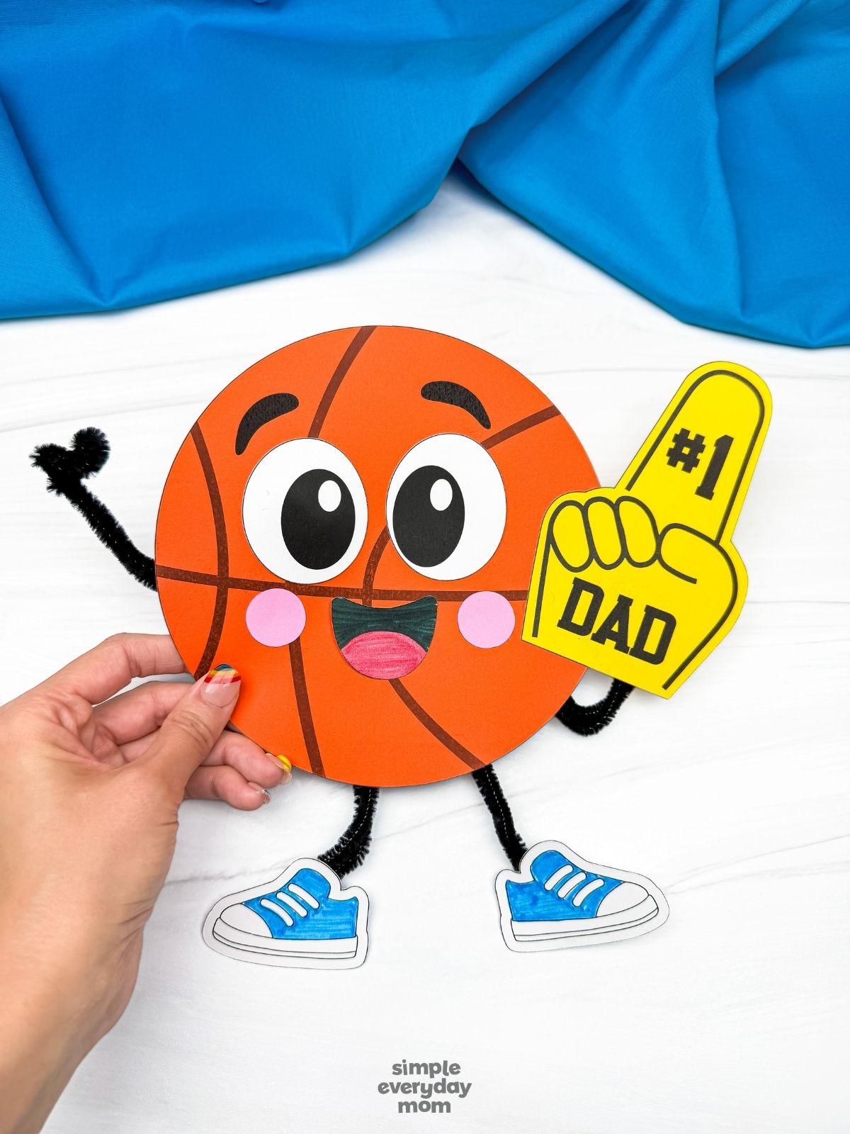 A completed craft of a basketball Father’s Day character holding a number one dad foam finger while a hand holds the craft.