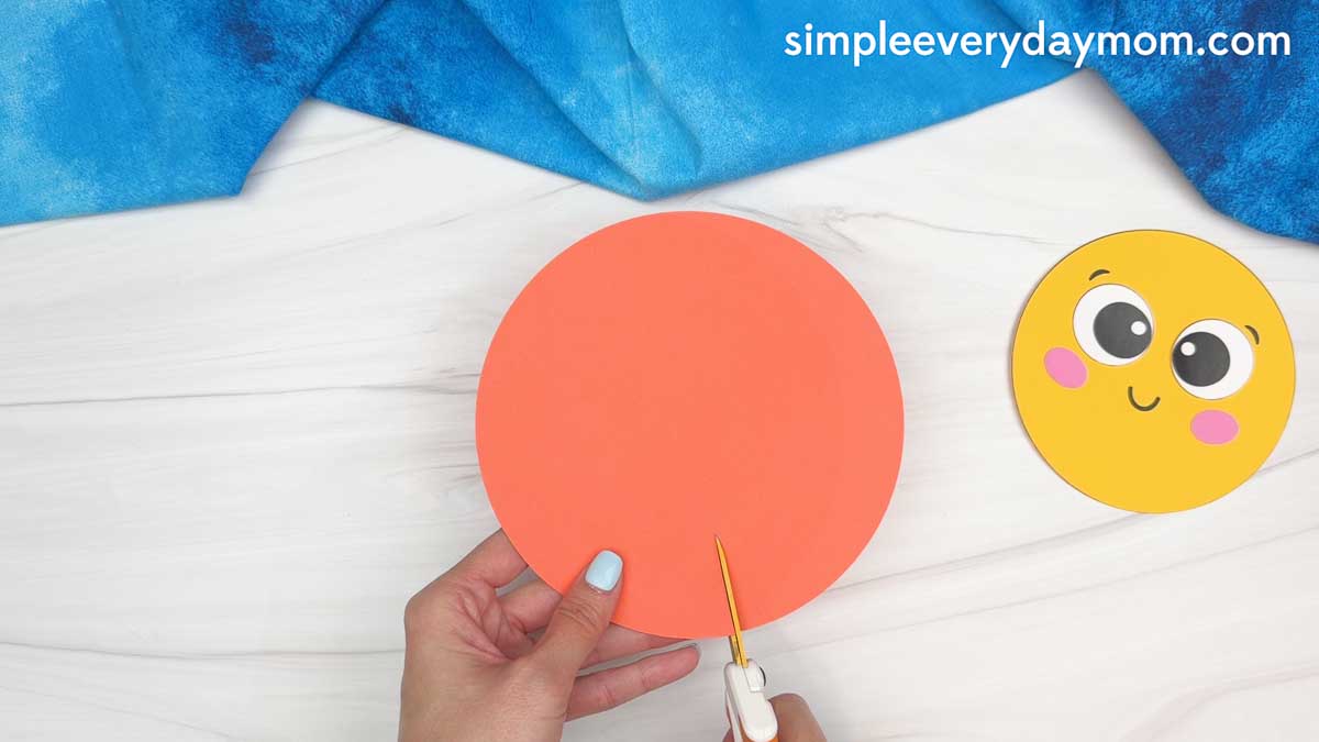 Hands cutting slits around an orange paper circle to create sun rays for a graduation craft