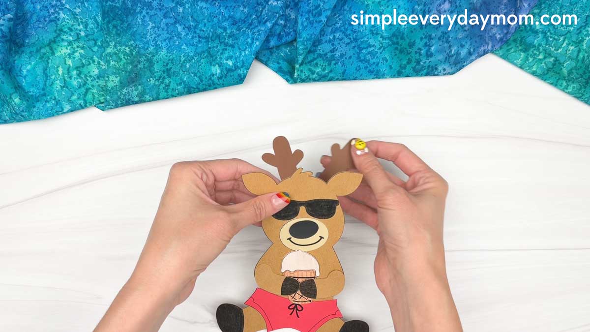 Hands attaching the reindeer's antlers to the head to complete a reindeer summer craft.
