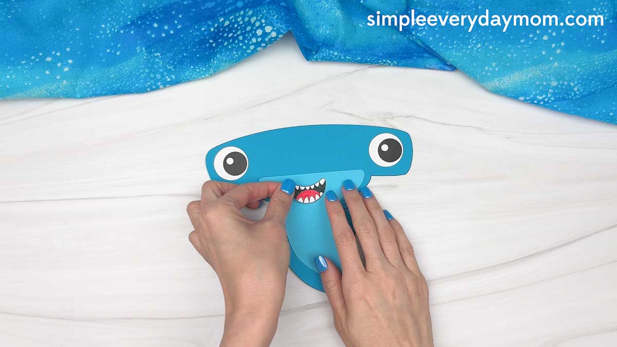 Hands attaching the shark's smiling mouth to a blue hammerhead shark craft.