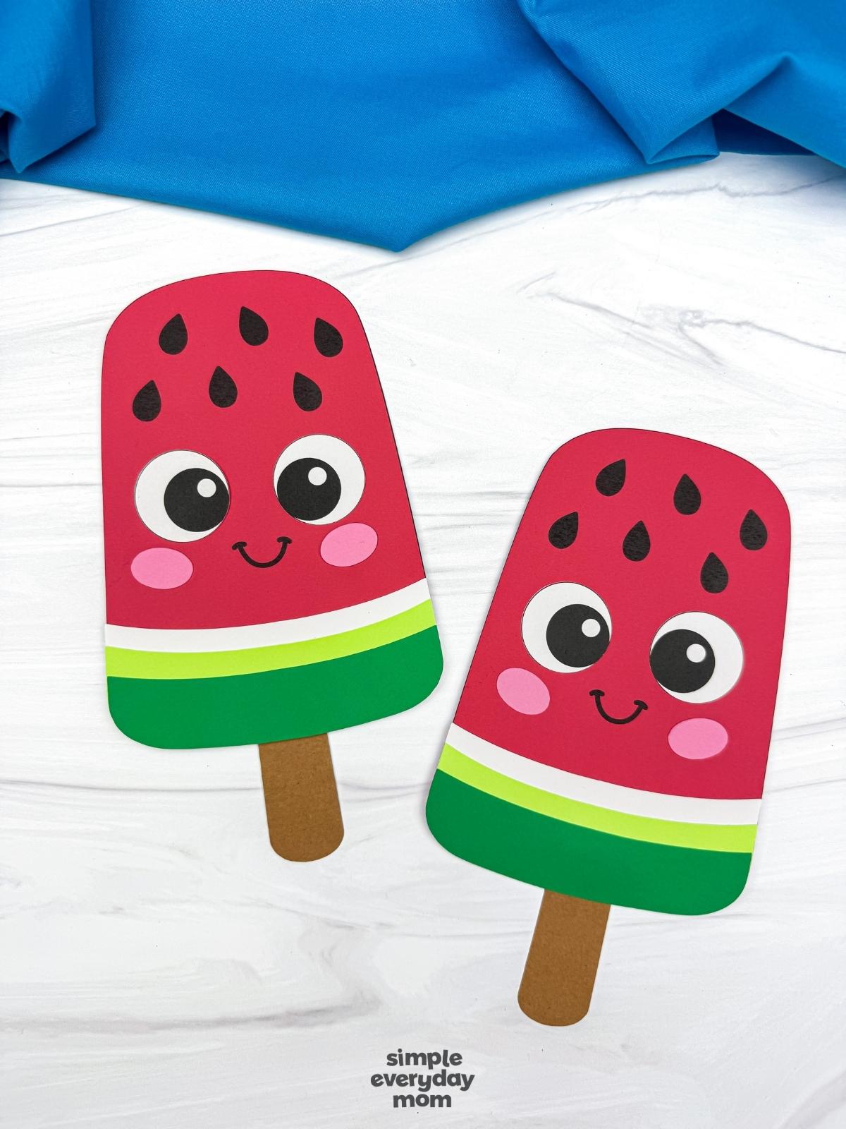 A completed craft showing two smiling watermelon popsicle crafts with popsicle stick handles on a white tabletop.