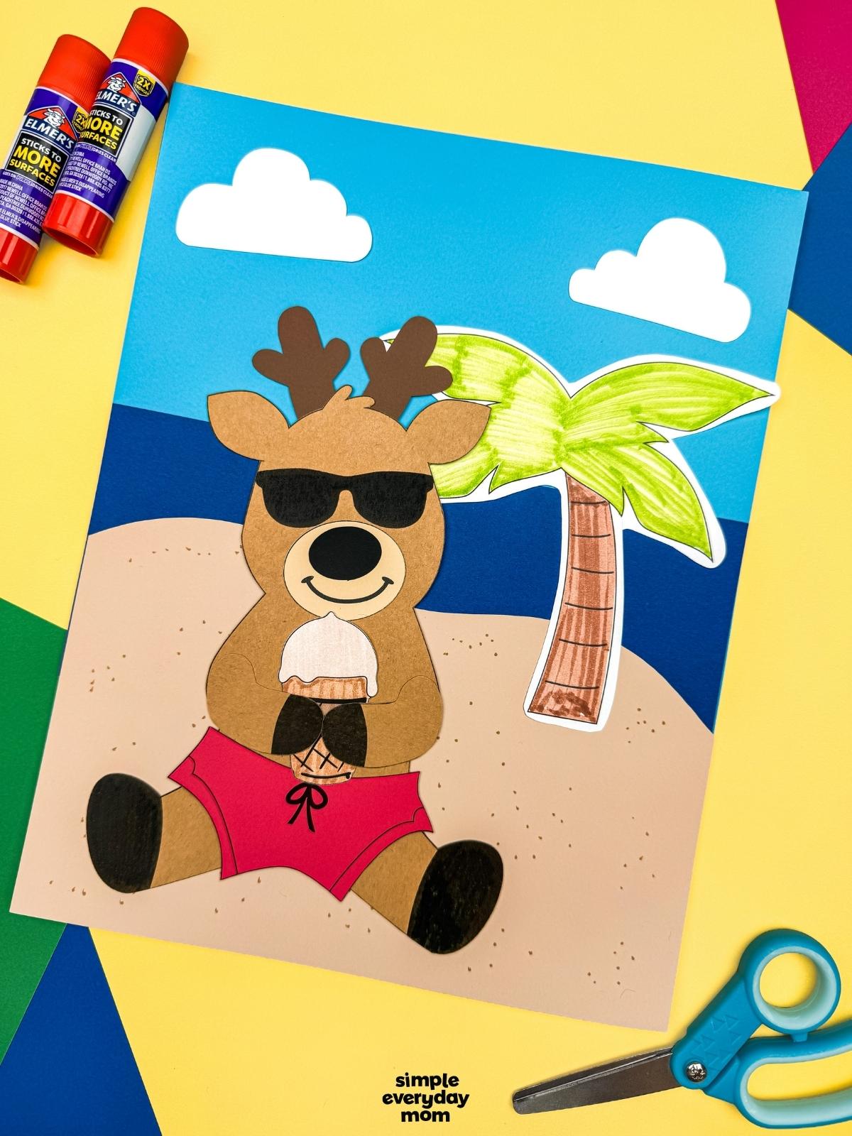 A completed craft featuring a reindeer in sunglasses and pink swim trunks holding an ice cream cone on a beach scene background with a palm tree and clouds.