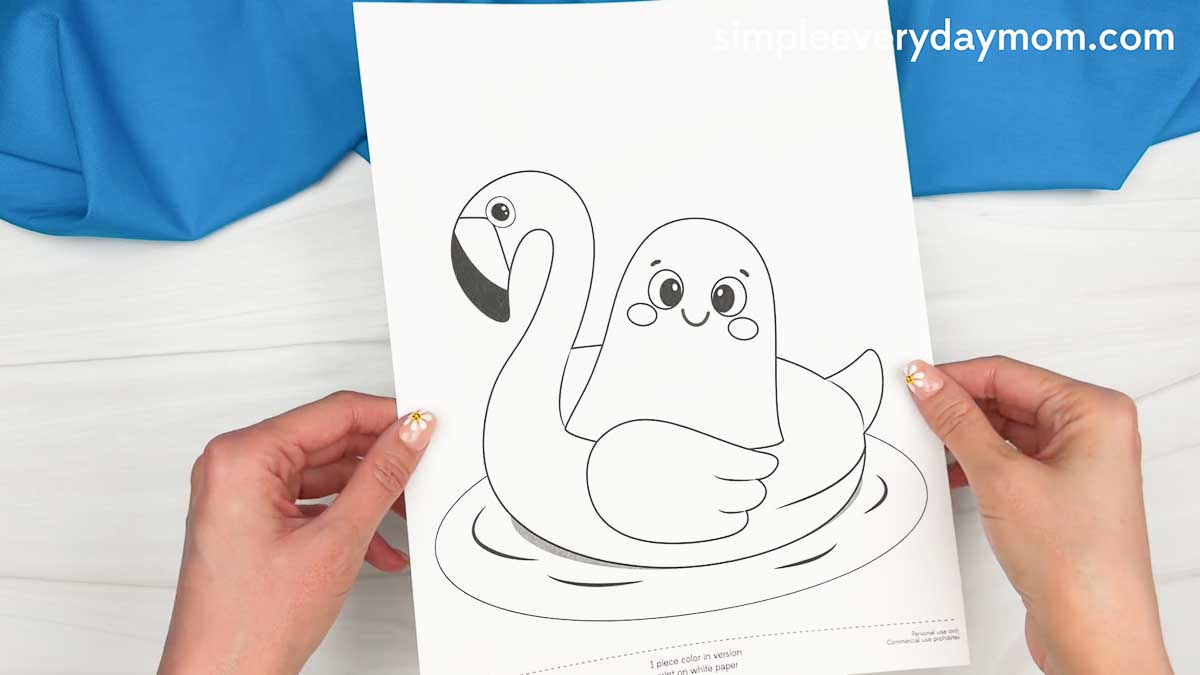 Hands holding a Summerween ghost craft template featuring a ghost in a flamingo pool float.
