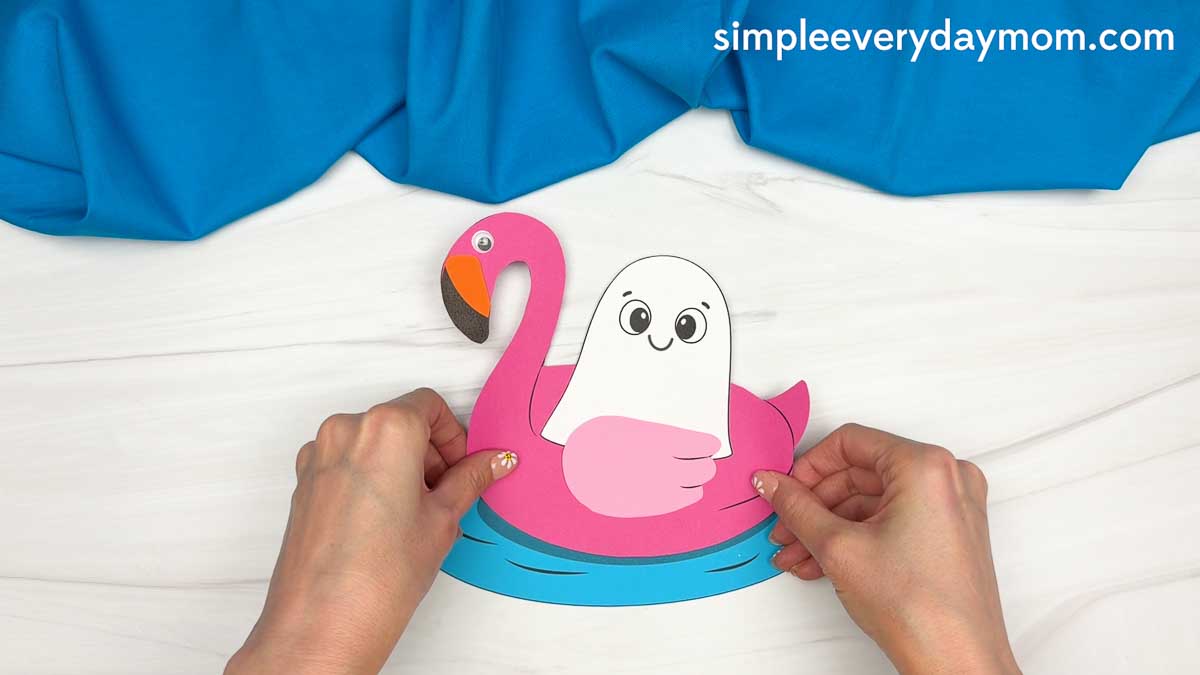 Hands holding the completed Summerween ghost craft with a ghost floating in a pink flamingo pool float.