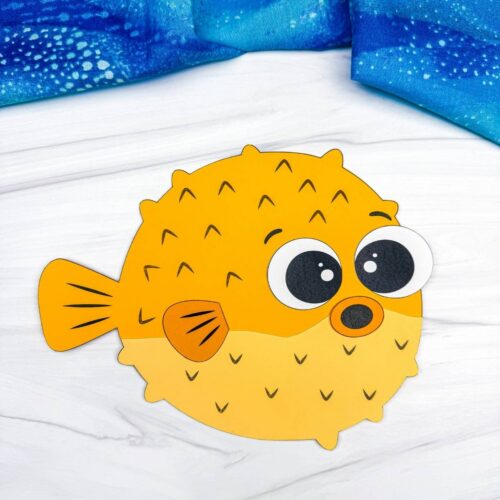 A completed craft featuring a yellow pufferfish paper craft with large eyes on a white tabletop.