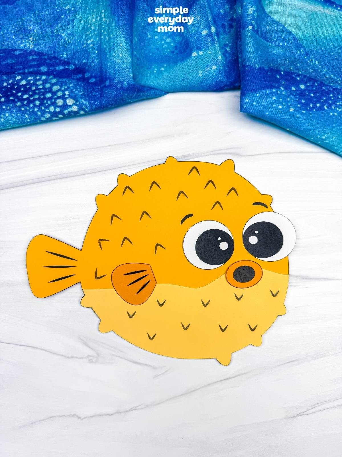 A completed craft featuring a yellow pufferfish paper craft with large eyes on a white tabletop.