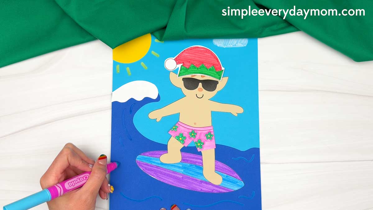 Hands drawing wave details around a surfing elf on a colorful ocean scene for an elf surfing craft.