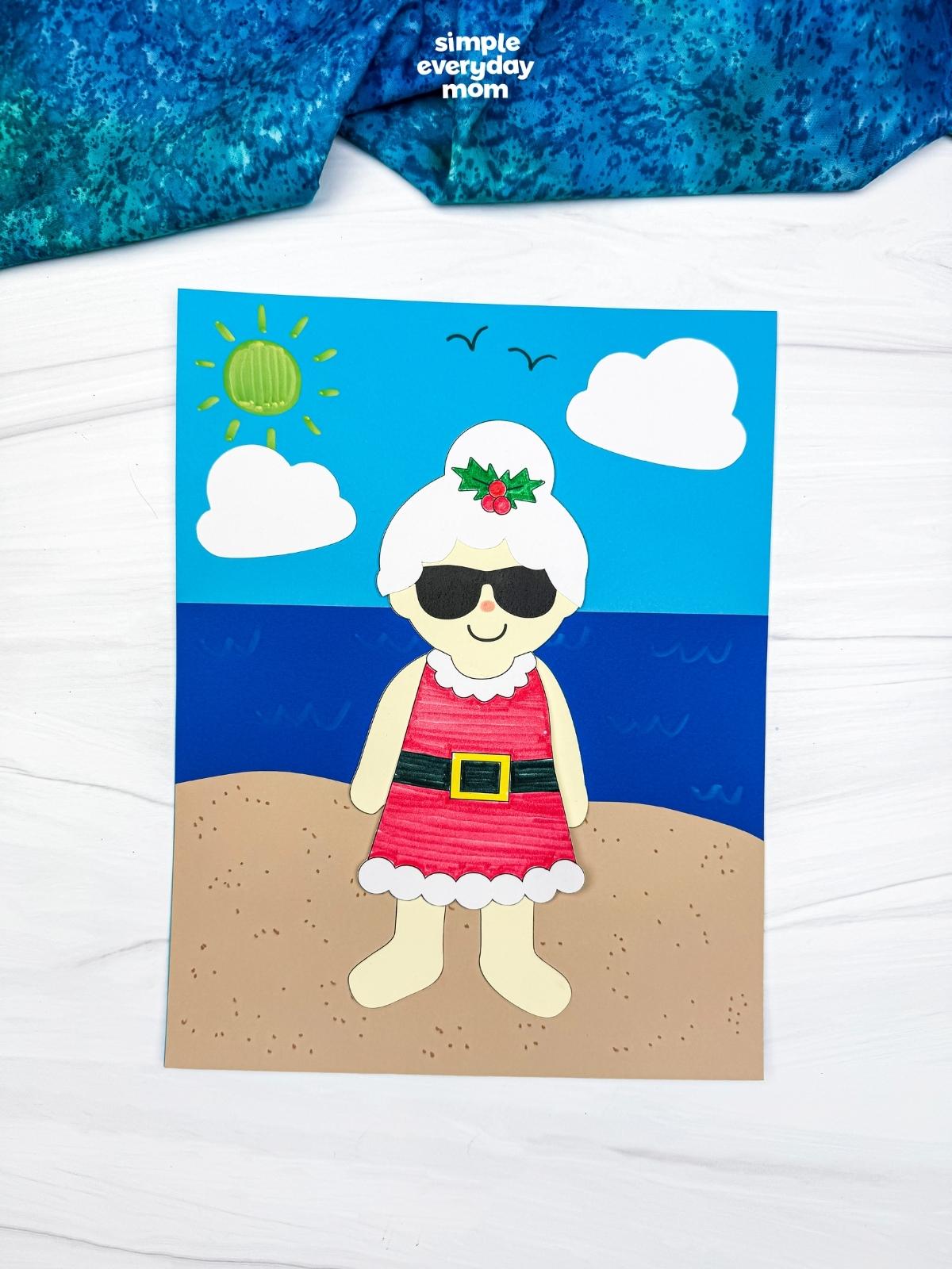 A completed craft of Summer Mrs. Claus standing on a sunny beach scene background.