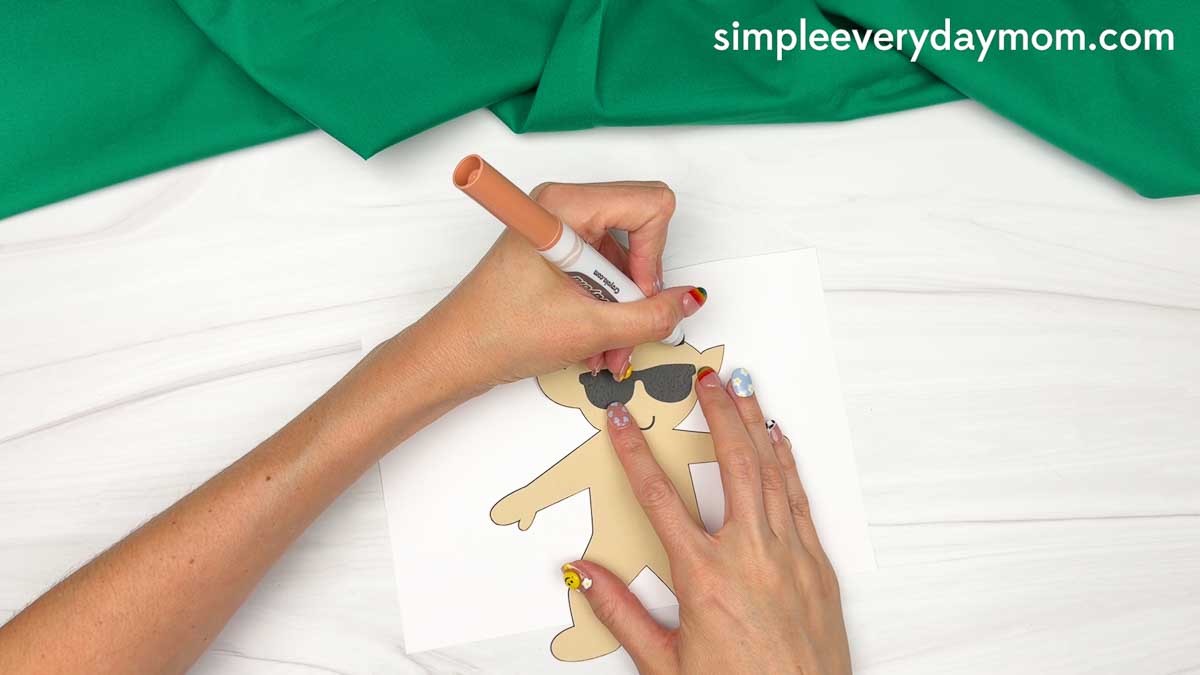 Hands coloring the face details on a cut out elf template wearing sunglasses for an elf surfing craft.