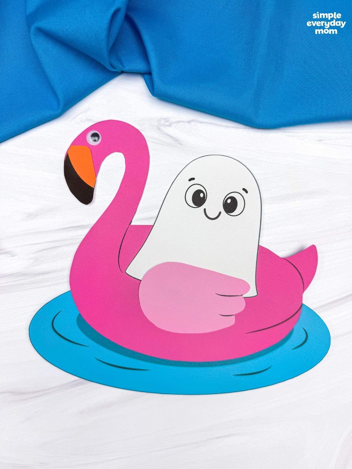 A completed craft featuring a ghost floating in a pink flamingo pool float on blue water.