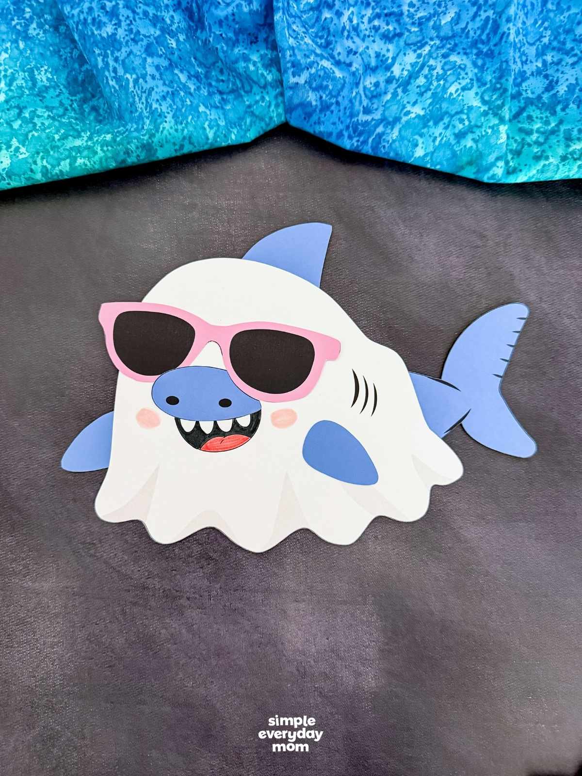 A completed craft of a Summerween ghost shark wearing pink sunglasses on a dark background.
