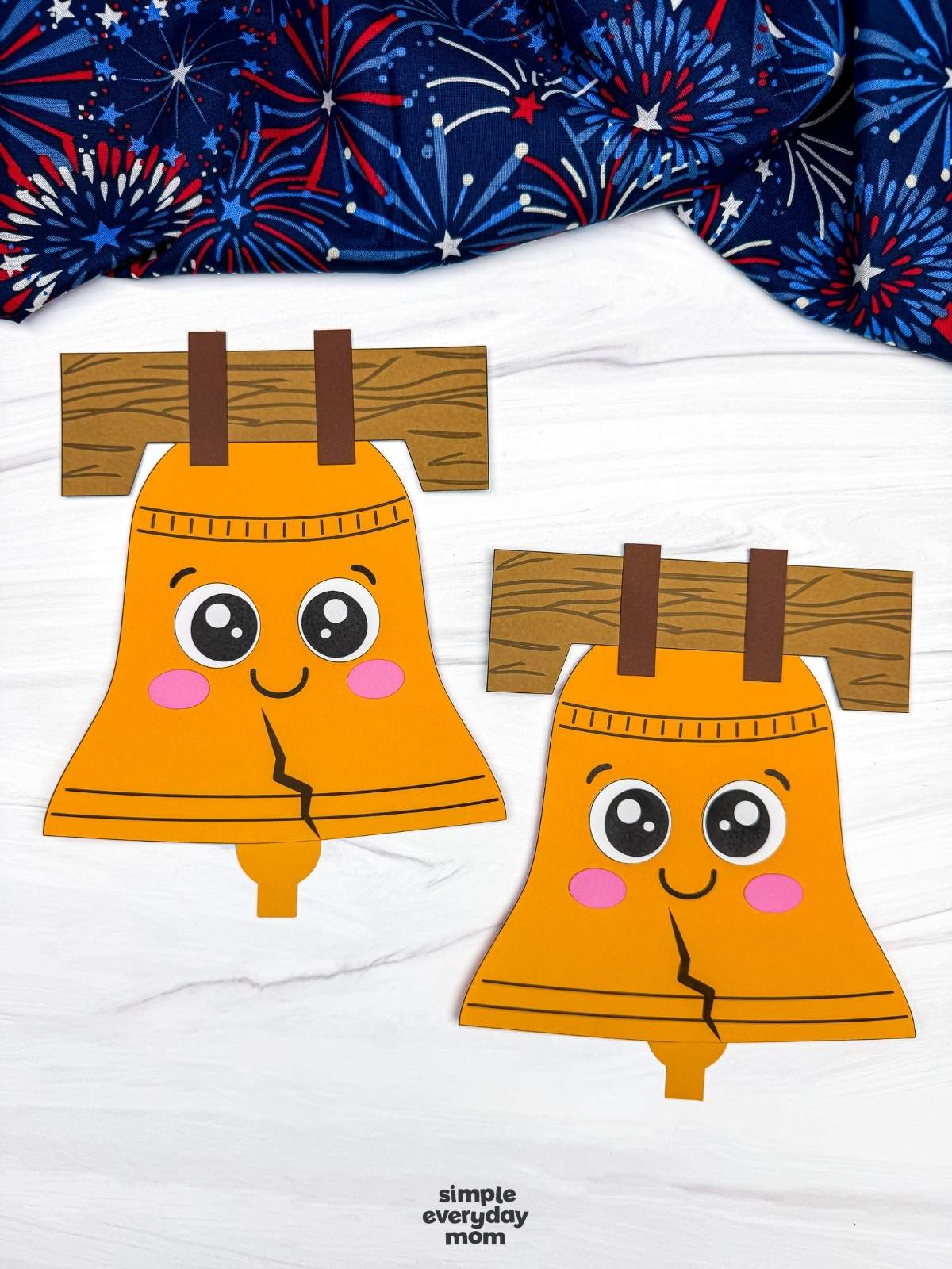 A completed Craft featuring two smiling Liberty Bell paper crafts with wood beams displayed on a tabletop.