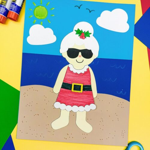 A completed craft of Summer Mrs. Claus on a beach scene with colorful paper, glue sticks, and scissors.