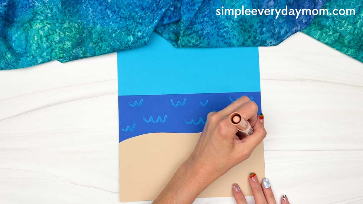 Hands drawing sand details on the beach scene background for the Summer Mrs. Claus craft.