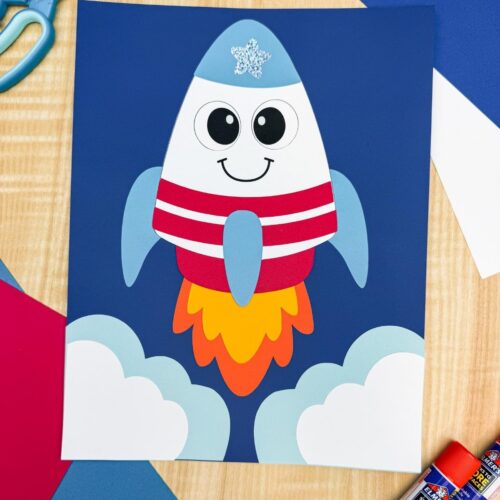 A completed 4th of July rocket craft launch scene with patriotic colors, fluffy paper clouds, colorful flame exhaust, and craft supplies.