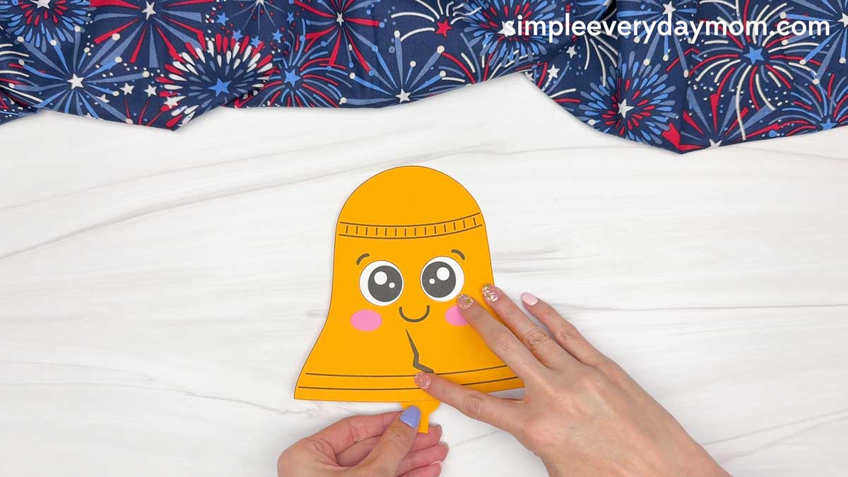 Hands attaching the bell clapper piece to the bottom of a Liberty Bell paper craft.