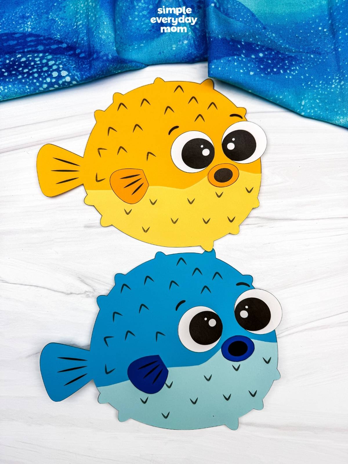 A completed craft featuring yellow and blue pufferfish paper crafts with large eyes on a white tabletop.