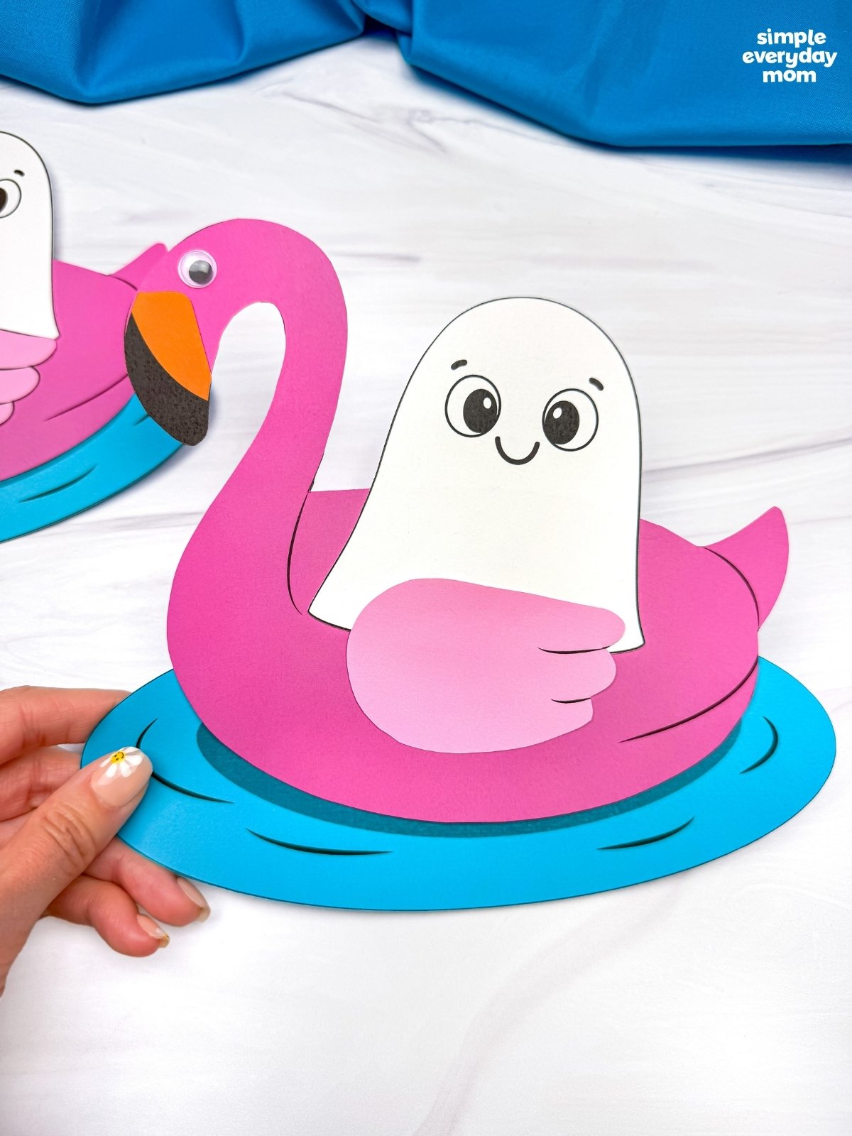 Hands holding a completed Summerween ghost craft featuring a ghost floating in a pink flamingo pool float.