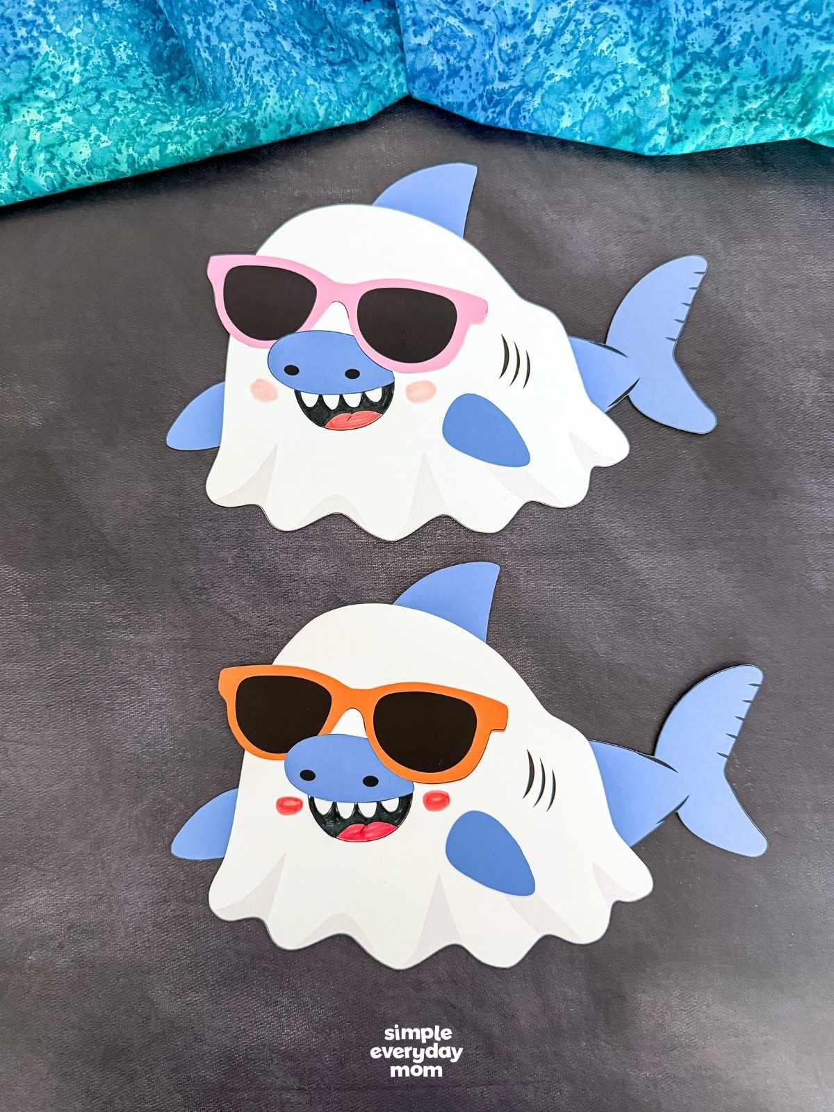 A completed craft of two Summerween ghost shark crafts wearing pink and orange sunglasses on a dark background.