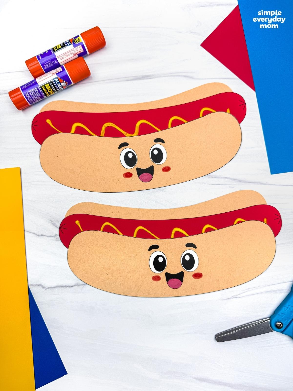 A completed Craft showing two smiling paper hot dog crafts surrounded by colorful craft supplies on a white tabletop.