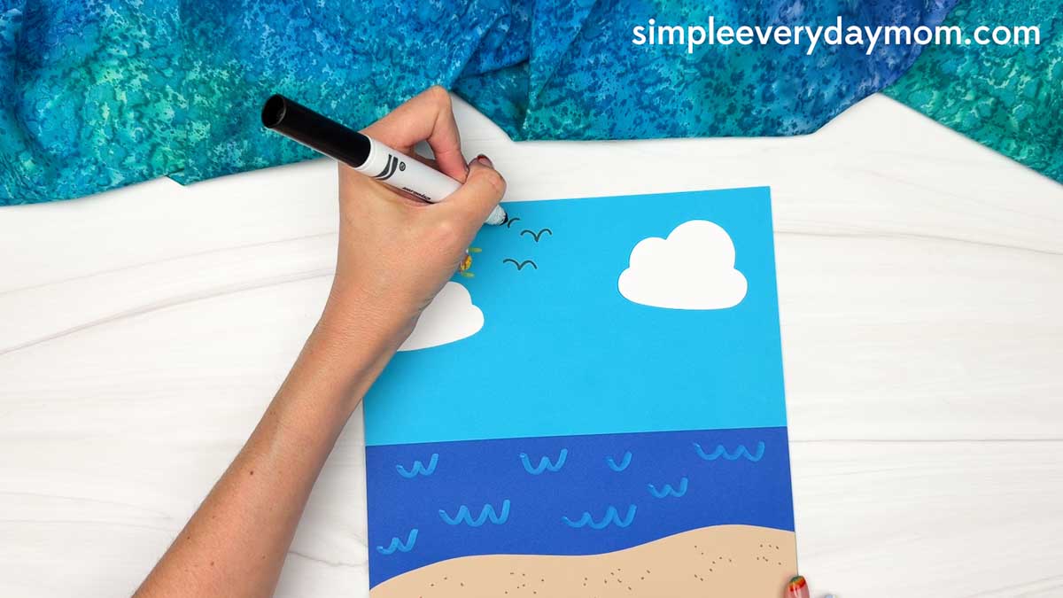 Hands drawing flying birds on the beach scene background for the Summer Mrs. Claus craft.